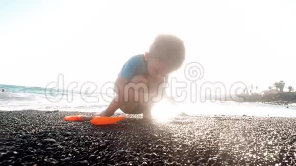 3岁小男孩在美丽的夕阳下在海边收集石头和海鳗的4K视频视频的预览图