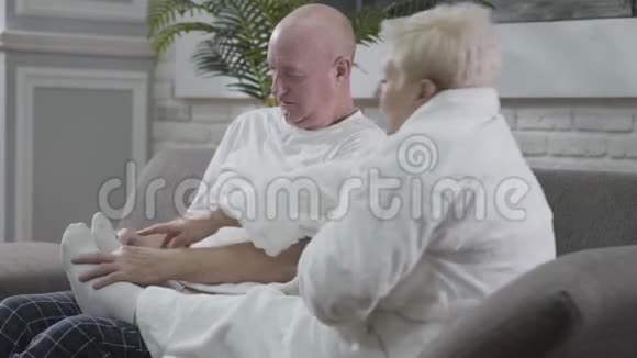 成熟的白种人男人坐在沙发上按摩妻子的脚丈夫照顾他可爱的孩子视频的预览图