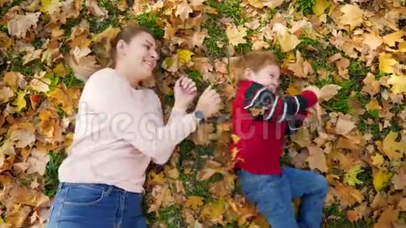 4k视频妈妈带着小儿子在草地上滚动上面覆盖着黄色落叶视频的预览图