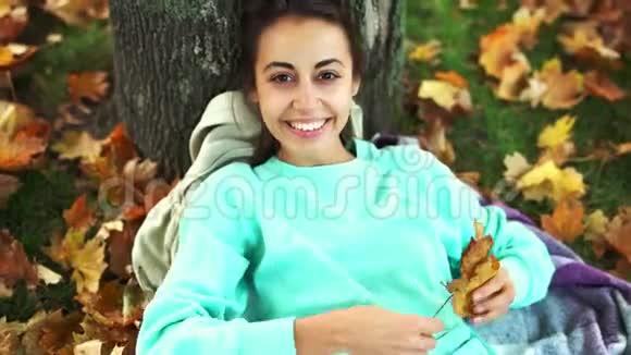 在秋天公园里美丽的年轻微笑的女人俯视着一片明亮的橙色叶子视频的预览图