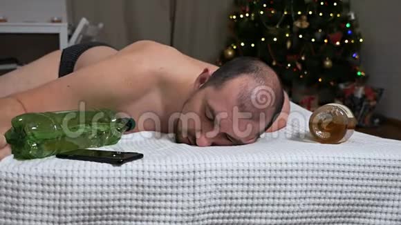 新年过后一个男人喝矿泉水在圣诞树上宿醉喝醉的男人视频的预览图