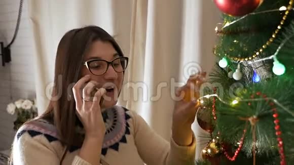 圣诞树附近的女人使用移动电话的漂亮女性收到新年的祝贺视频的预览图