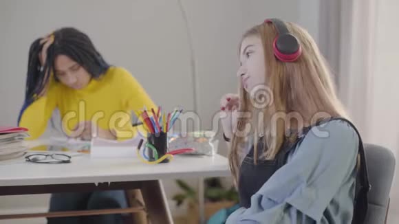 开朗的白种人女孩戴着耳机拿着朋友的笔记本笑着非裔美国青少年试图得到笔记视频的预览图