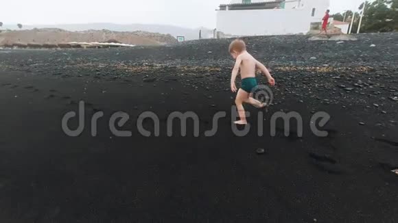 4k视频可爱的小男孩和美丽的年轻妈妈在黑色的火山沙海滩上奔跑和玩耍视频的预览图