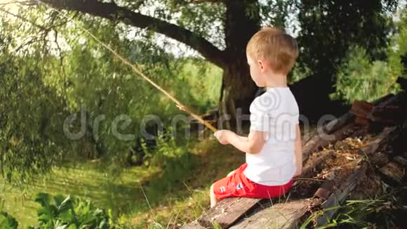 幼儿小男孩坐在湖边用自制鱼竿钓鱼的4k视频视频的预览图