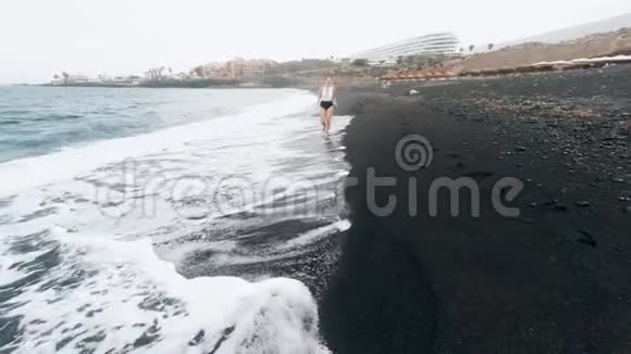 4k视频快乐快乐美丽的女人在黑色火山海滩上奔跑视频的预览图