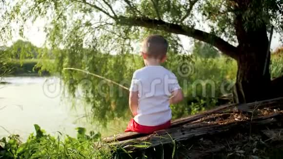 可爱的幼儿男孩用旧木棒在池塘里钓鱼的4k视频视频的预览图