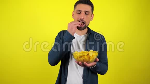 一个穿着蓝色衬衫和白色T恤的年轻人吃辛辣的薯片用一杯水把它们熄灭视频的预览图