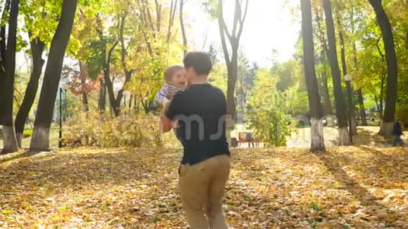 快乐的年轻父亲抱着他的小儿子在秋天的公园里围着他转视频的预览图