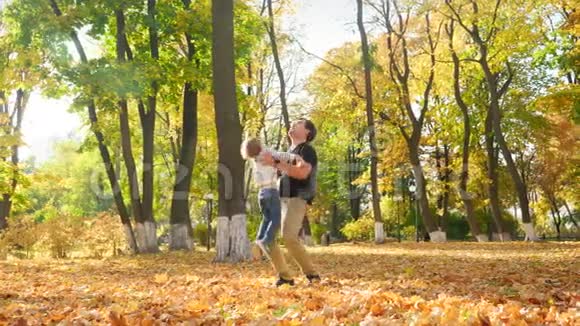 4k视频快乐的年轻父亲和他的小儿子在秋天公园的空中玩耍视频的预览图