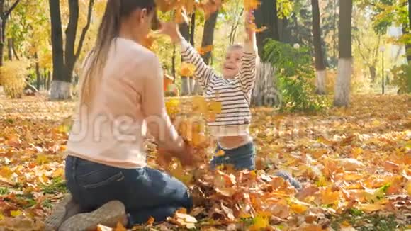 4k视频快乐男孩与母亲坐在秋天公园抛洒金色树叶视频的预览图
