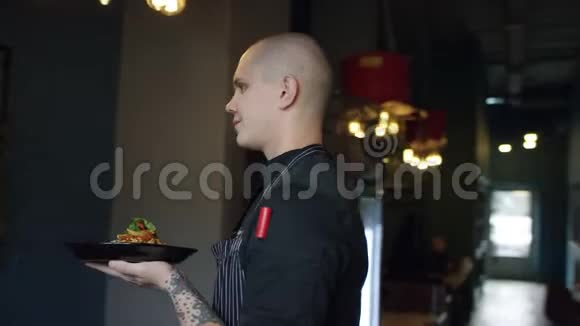 年轻的厨子站在餐厅里拿着盘子和意大利面跟踪360度的弧线射击视频的预览图