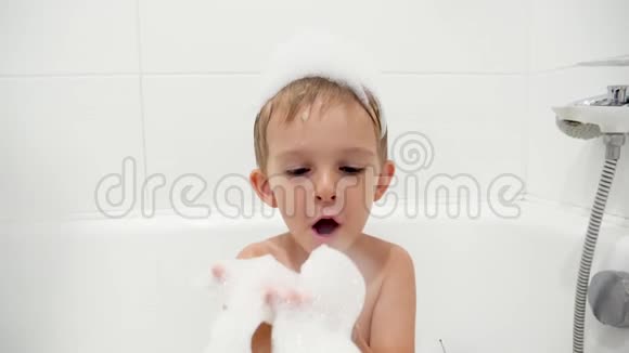特写慢镜头视频快乐的微笑男孩洗澡时洗澡相机吹肥皂泡沫视频的预览图