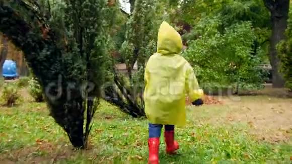 雨后穿着黄色雨衣和红色胶靴的小男孩在秋天公园奔跑快乐地笑着视频的预览图