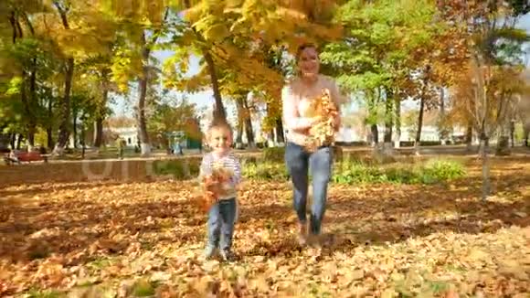 4k镜头快乐的母亲和4岁的小儿子在公园里奔跑在镜头里扔秋叶视频的预览图