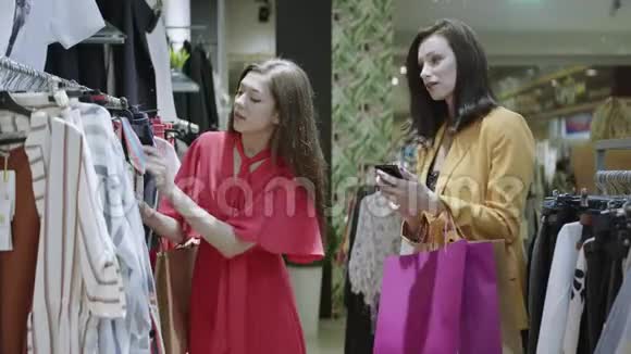 拿着购物袋时髦的黑发女人正在拍她的朋友在商店里试衣服的照片粉红少女视频的预览图