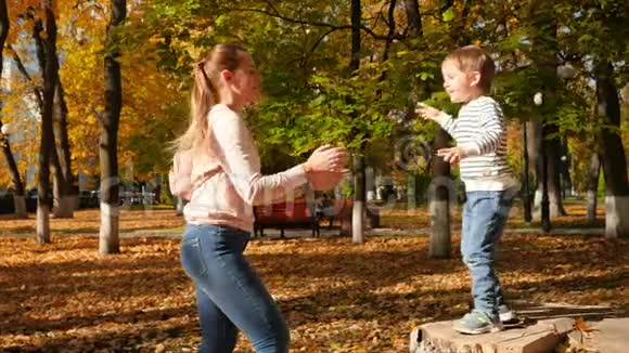 4k视频快乐的笑着年轻的妈妈在秋天的公园里跳了起来旋转了他视频的预览图