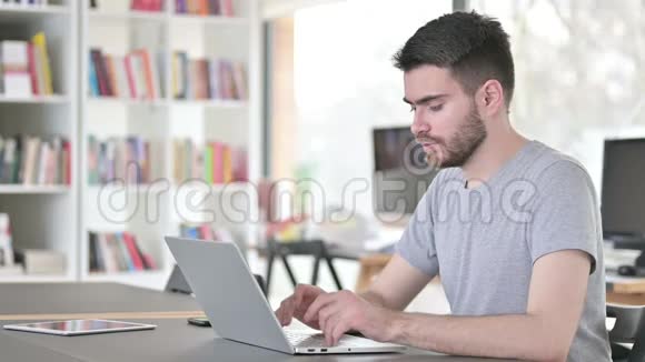 头痛的年轻人在办公室用笔记本电脑视频的预览图