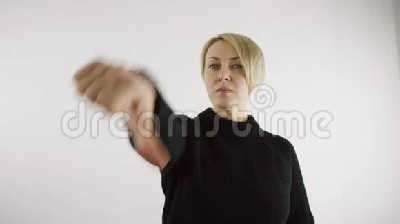成年白种人金发女性在明亮的室内白色背景上做拇指向下的手势视频的预览图
