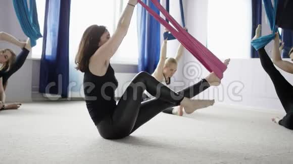 一群年轻的美女在健身俱乐部的紫色吊床上做空中瑜伽练习视频的预览图