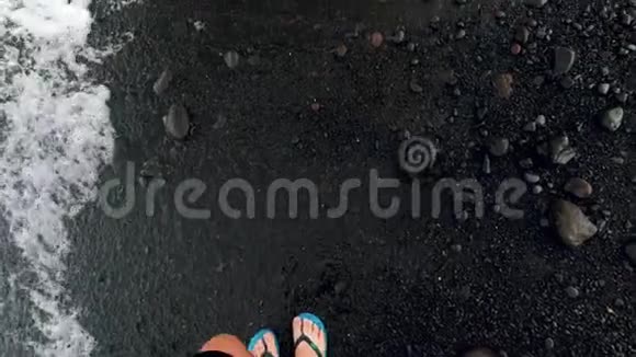 在黑色火山沙滩和海浪上行走的人脚拖鞋中的4k慢动作视频视频的预览图