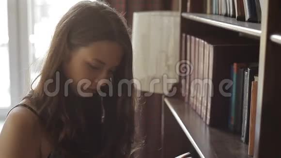 漂亮的年轻女子正在图书馆书架上挑选一本教科书视频的预览图