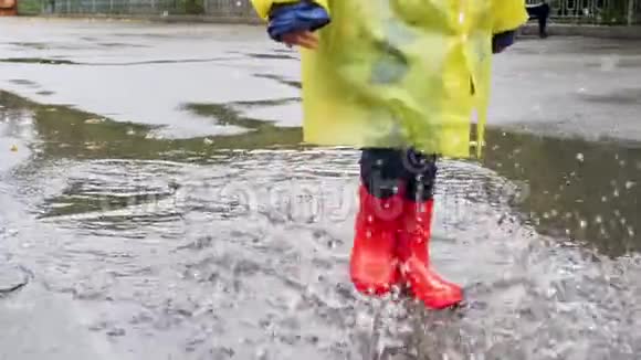 慢动作特写视频儿童穿红色橡胶靴在公园的大水坑上行走溅水儿童视频的预览图