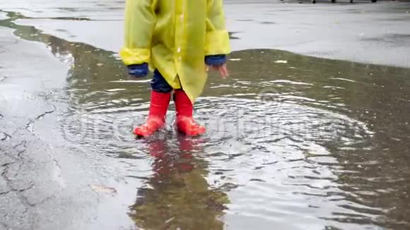 穿红色橡胶靴的小孩在街上雨后在大水坑里泼水和跳跃的慢动作视频视频的预览图