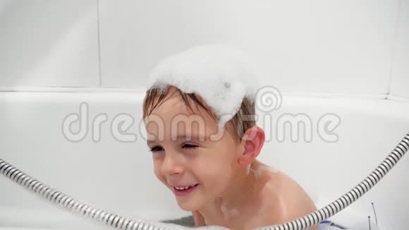 慢动作视频快乐微笑的小男孩洗澡时用洗发水洗头视频的预览图