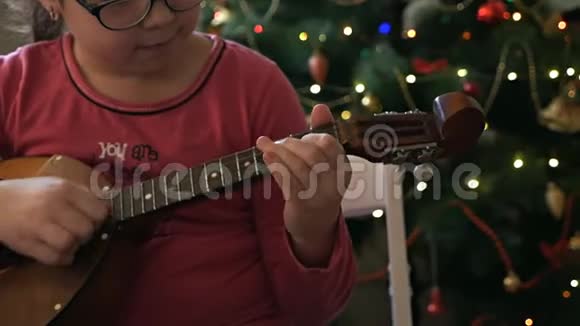 女孩在一棵装饰的圣诞树的背景下扮演多姆布拉视频的预览图