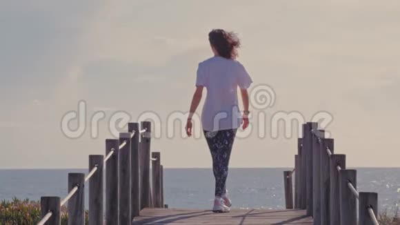 快乐的女人手臂举在海边的木制步行者视频的预览图
