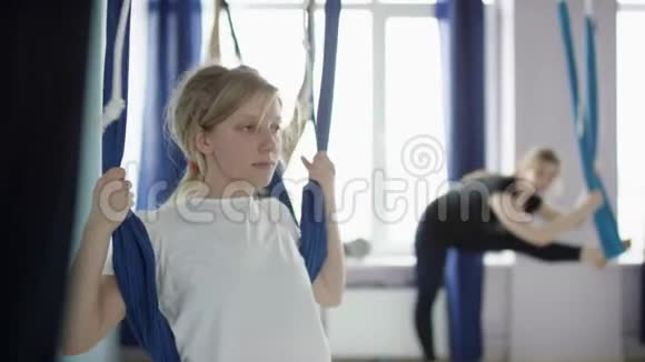 运动胸罩和紧身衣上的年轻美女使用空中瑜伽吊床做反重力的腿部热身运动视频的预览图