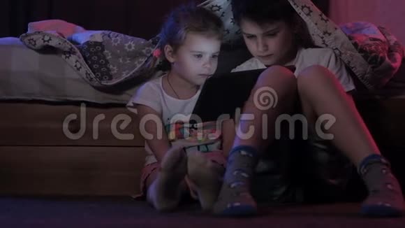 男孩和小女孩坐在床边的地板上卧室里的平板电脑视频的预览图
