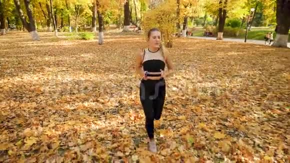 4K慢动作视频由高点美丽的年轻女子腿部慢跑在秋季公园和听音乐视频的预览图