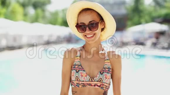 美丽的微笑女子比基尼帽子和太阳镜摆在明亮的夏天背景视频的预览图