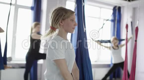 金发女人做伸展运动的腿使用吊床空中瑜伽课堂上的女性小组练习视频的预览图