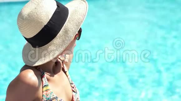 特写美丽的白种人女孩戴着帽子坐在池边清澈的蓝色水背景和日光浴视频的预览图