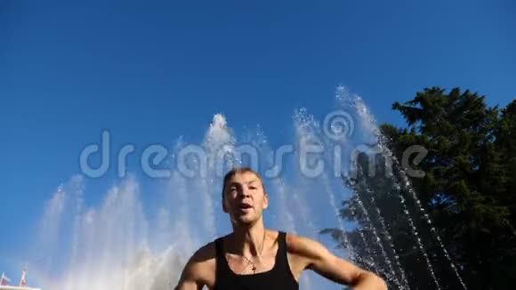 一个年轻快乐的家伙跳着现代芭蕾在一个夏天公园的喷泉的背景下摇摇晃晃缓行视频的预览图