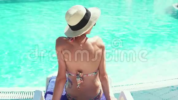 年轻女士穿比基尼和帽子在池边背景的桌椅上放松视频的预览图