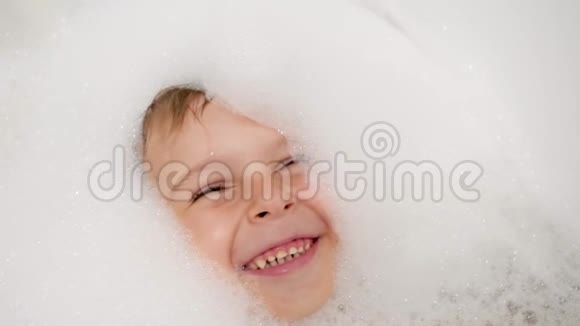 4k特写慢动作视频欢快微笑的小男孩躺在浴缸里用肥皂泡沫视频的预览图