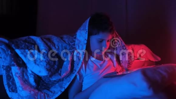 男孩坐在卧室的地板上睡在霓虹灯红色蓝光下看上去像平板电脑视频的预览图