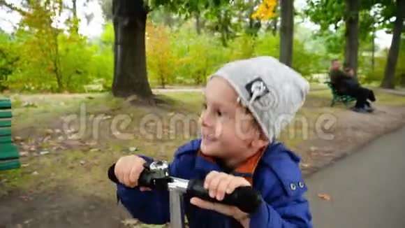 秋天公园里快乐的微笑着的小男孩骑着滑板车快速前进视频的预览图