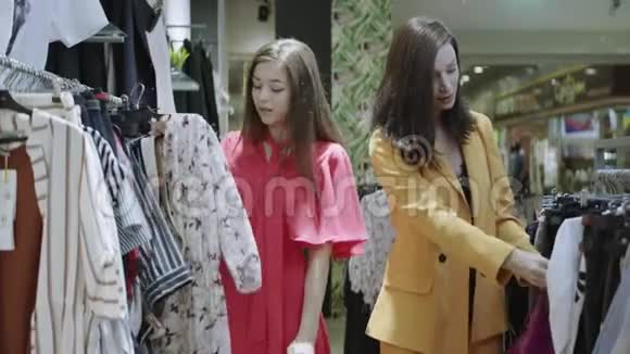 衣服店里的两个漂亮时髦的女人中有一个正在看夹克另一个穿粉色连衣裙的女孩发现了花视频的预览图