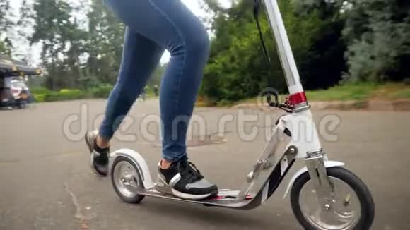 特写4k视频女性脚站在滑板车上骑在公园的小路上视频的预览图