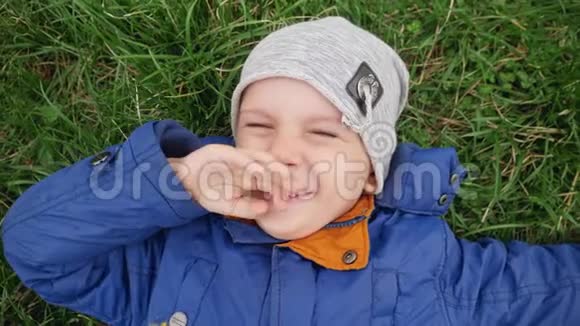 特写4k视频快乐微笑的小男孩躺在公园的绿草上抬头看着镜头视频的预览图