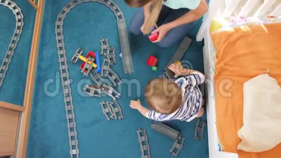 从高角度看小男孩和年轻母亲在地板上玩耍和组装玩具铁路视频的预览图