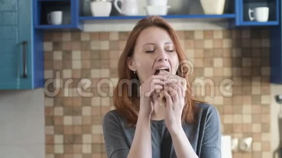 饥饿的女孩在家咬三明治早上在厨房吃早餐视频的预览图