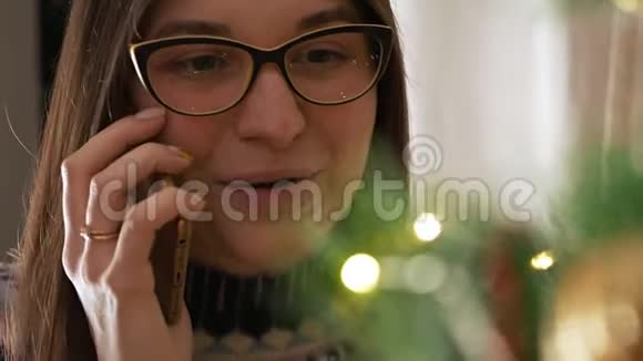 圣诞树附近的女人漂亮的女性使用手机获得新年祝贺年轻女子视频的预览图