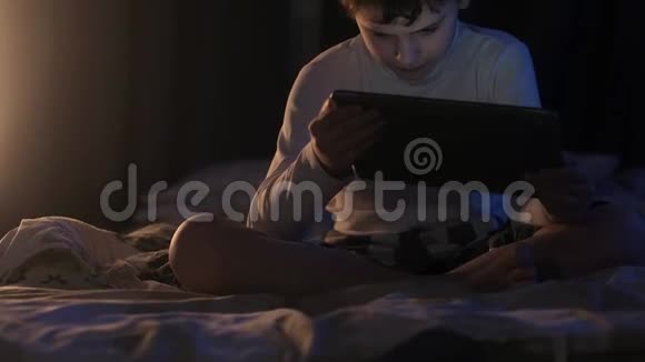晚上男孩在卧室里看平板电脑上的卡通片视频的预览图