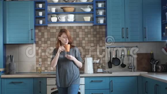 年轻漂亮的红发女孩正在现代厨房里喝早咖啡视频的预览图